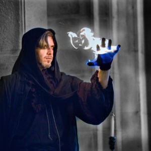 Artista vestido con túnica oscura realizando un espectáculo de magia con fuego azul en la palma de su mano.