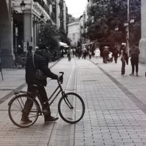 Hombre mayor con gorra y chaqueta empujando su bicicleta por una calle peatonal del centro de Logroño, rodeado de gente caminando.