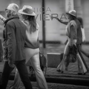 Pareja caminando por la calle, mientras la mujer señala una cristalera que refleja su imagen y la del entorno con nitidez.