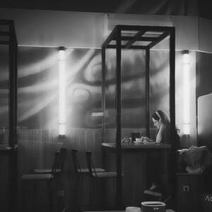 Joven sentada sola en una mesa de cafetería con auriculares puestos, concentrada en escribir o leer, bajo una tenue luz interior.